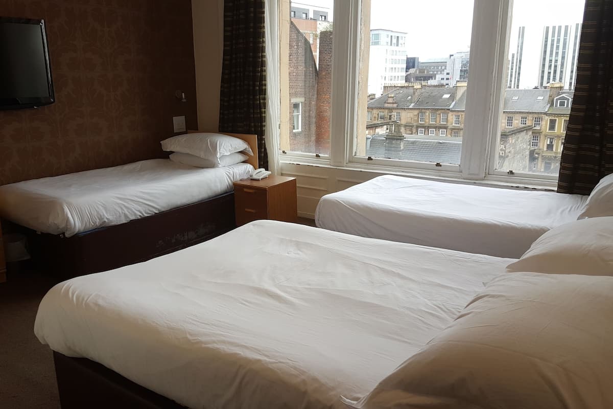 A hotel room with two single beds, a wooden dresser, a flat-screen TV mounted on the wall, and a window with a city view.