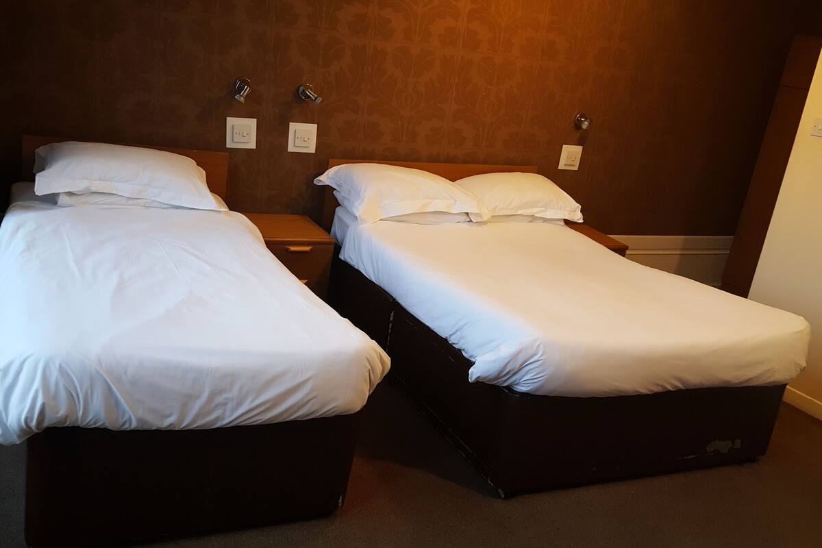 A hotel room with two single beds, a nightstand, and a wall socket.