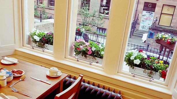 Un'area pranzo con un tavolo apparecchiato per due persone, un termosifone e una finestra vista sulla strada e sugli edifici.
