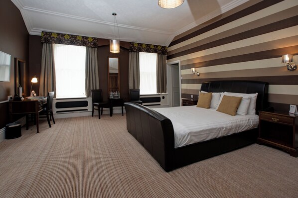 Habitación de hotel con una cama grande, un escritorio y una silla. Cuenta con una ventana con cortinas, un espejo y una lámpara.