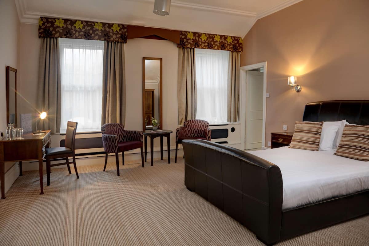 A hotel room with a bed, a desk, two chairs, a small table, and a mirror.