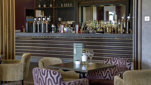 A bar area with a counter, shelves of bottles, a mirror, and patterned chairs.