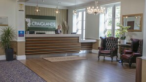 A reception area with a reception desk, two upholstered chairs, a chandelier, and a large window.