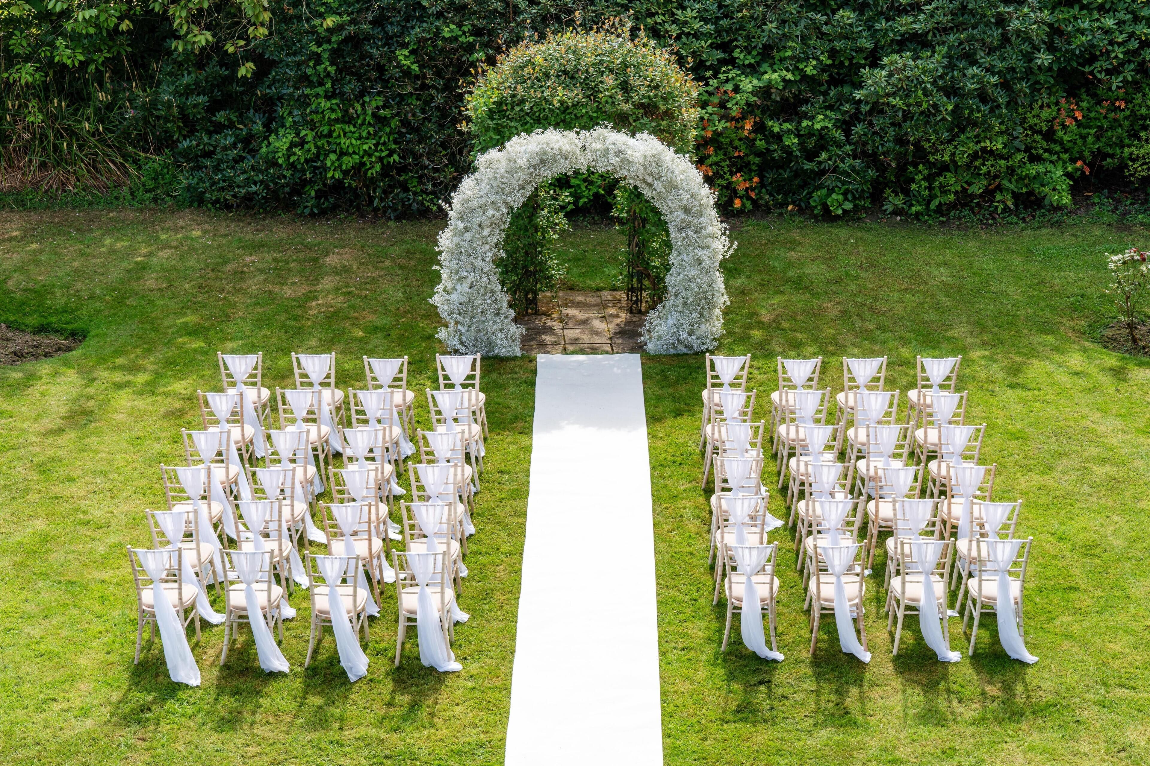 Une cérémonie de mariage en plein air, avec une allée blanche et des chaises disposées de part et d’autre.