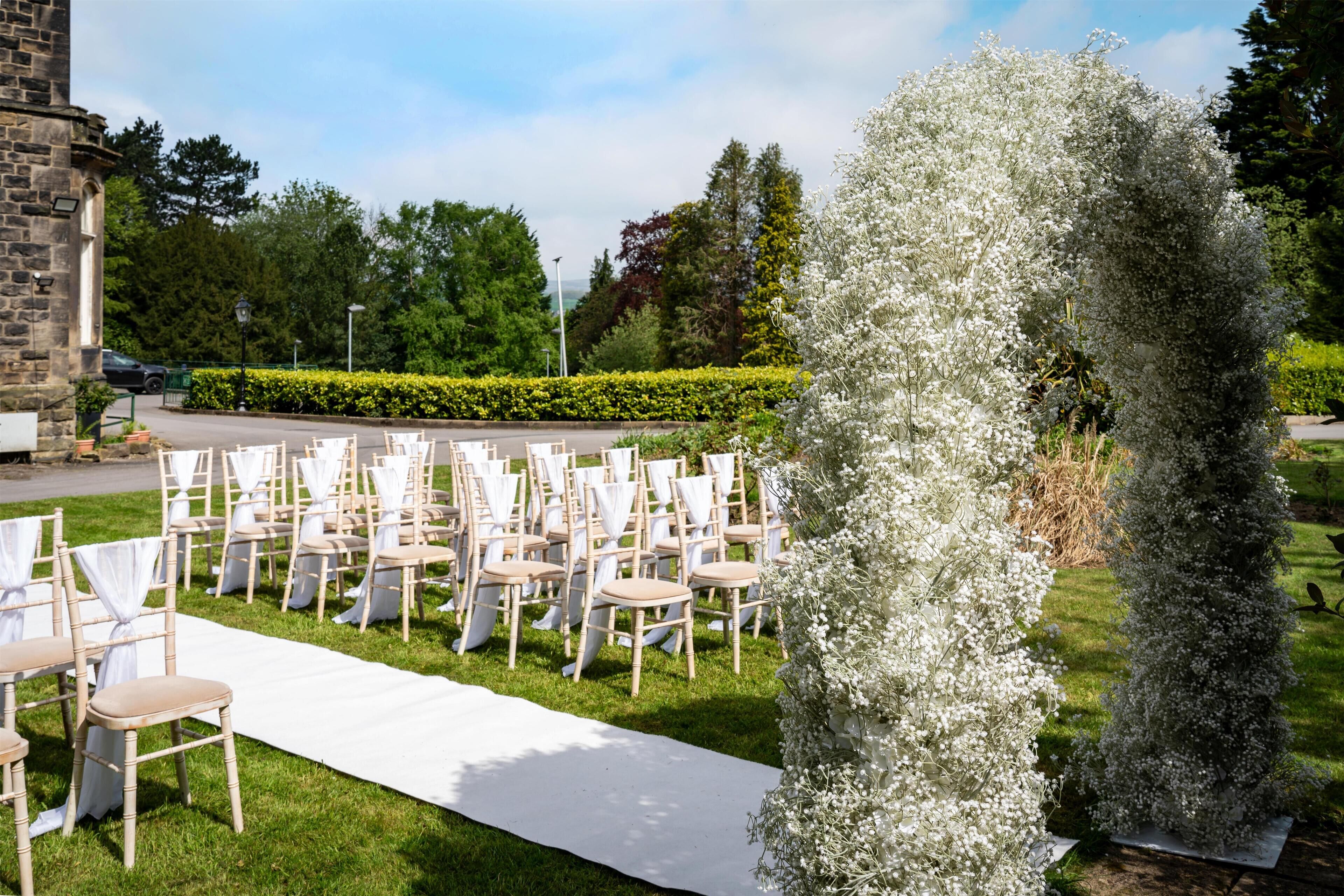 Montaje de boda al aire libre con filas de sillas blancas y un pasillo cubierto con una alfombra blanca.