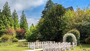 A wedding ceremony setup with chairs arranged in rows, a white aisle, and a natural backdrop of trees and shrubs.