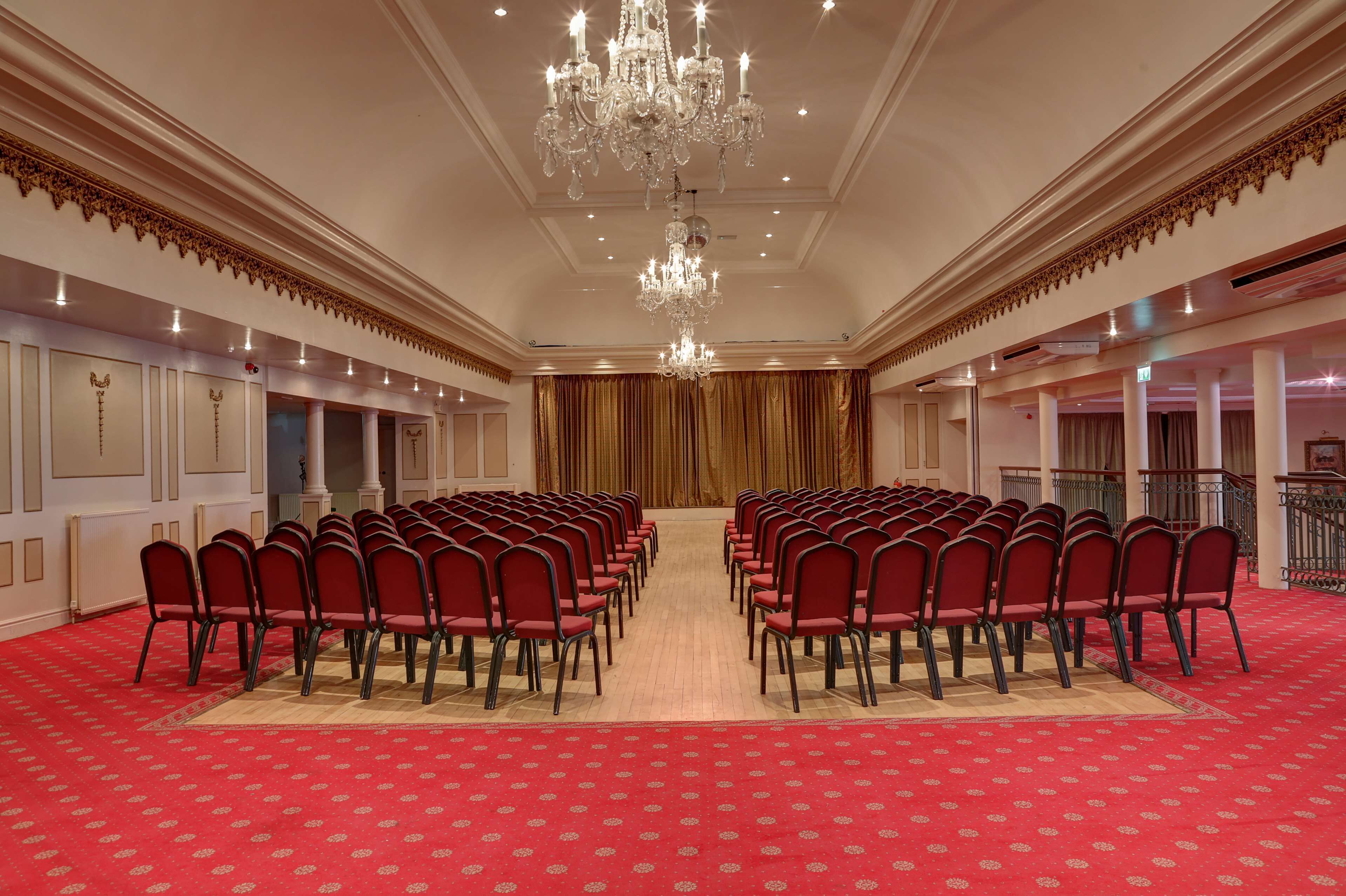 Une salle de conférence avec des rangées de chaises rouges, un lustre et une moquette rouge.