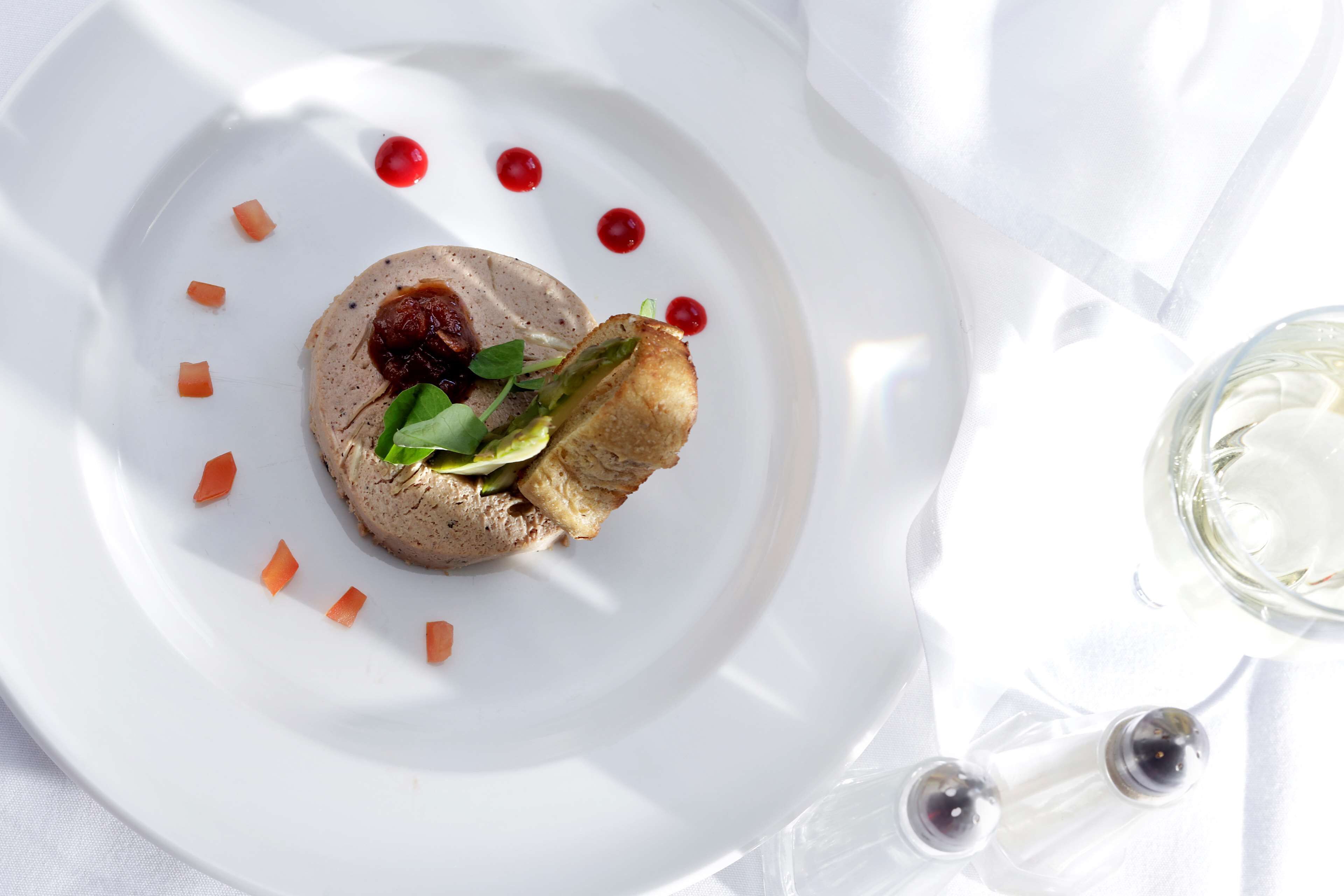 A white plate with a food item, garnished with small red dots and carrot pieces, on a white tablecloth.
