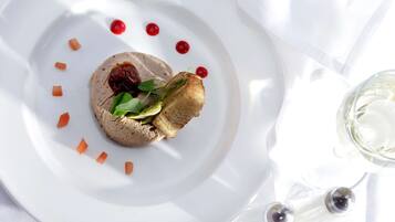 A white plate with a food item, garnished with small red dots and carrot pieces, on a white tablecloth.