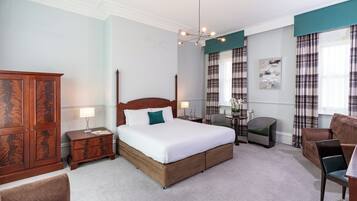 A hotel room with a large bed, a wooden wardrobe, a desk with a chair, and a sofa.