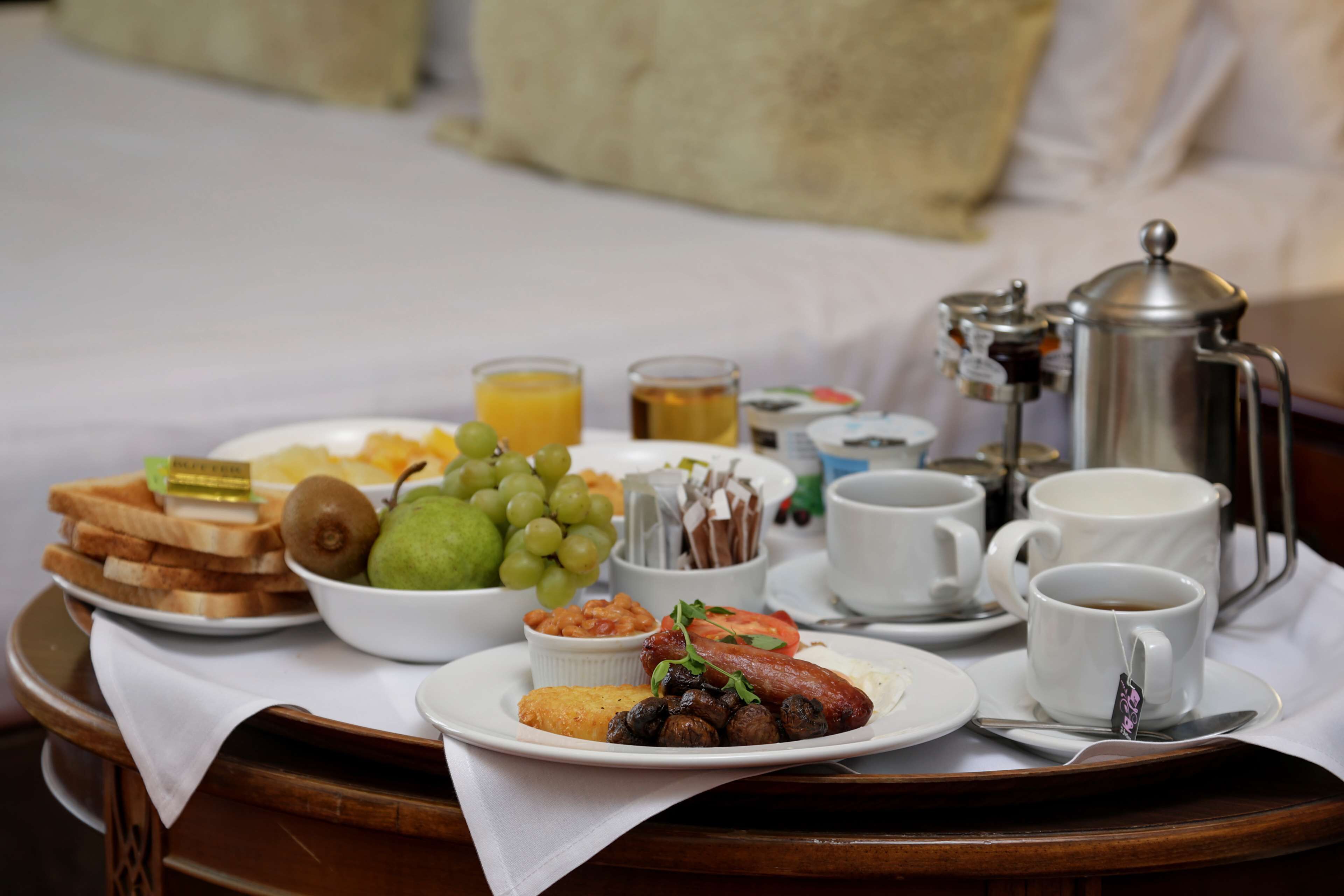 A breakfast tray with toast, fruit, eggs, and coffee on a bed.