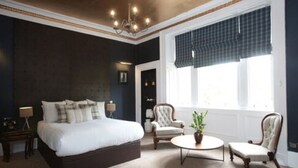 Une chambre à coucher avec un grand lit, deux fauteuils, une table basse ronde et un lustre.