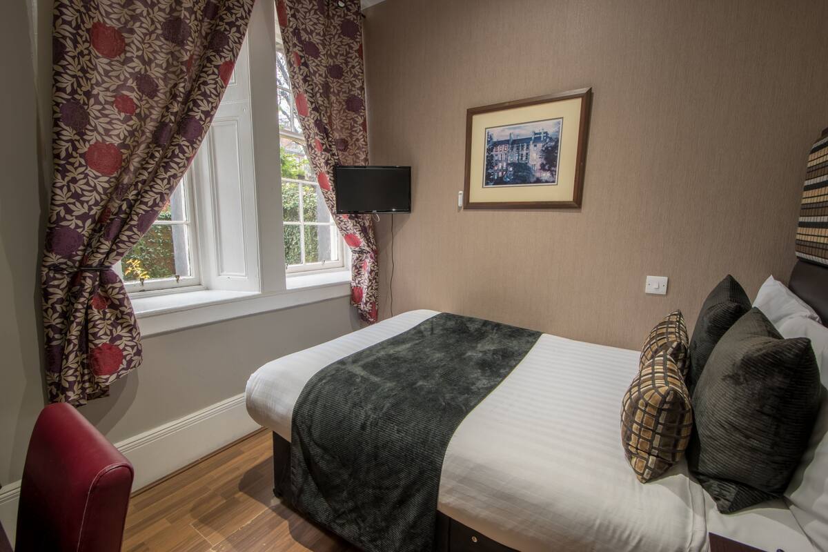 A bedroom with a bed, a TV, a framed picture, and a window with curtains.