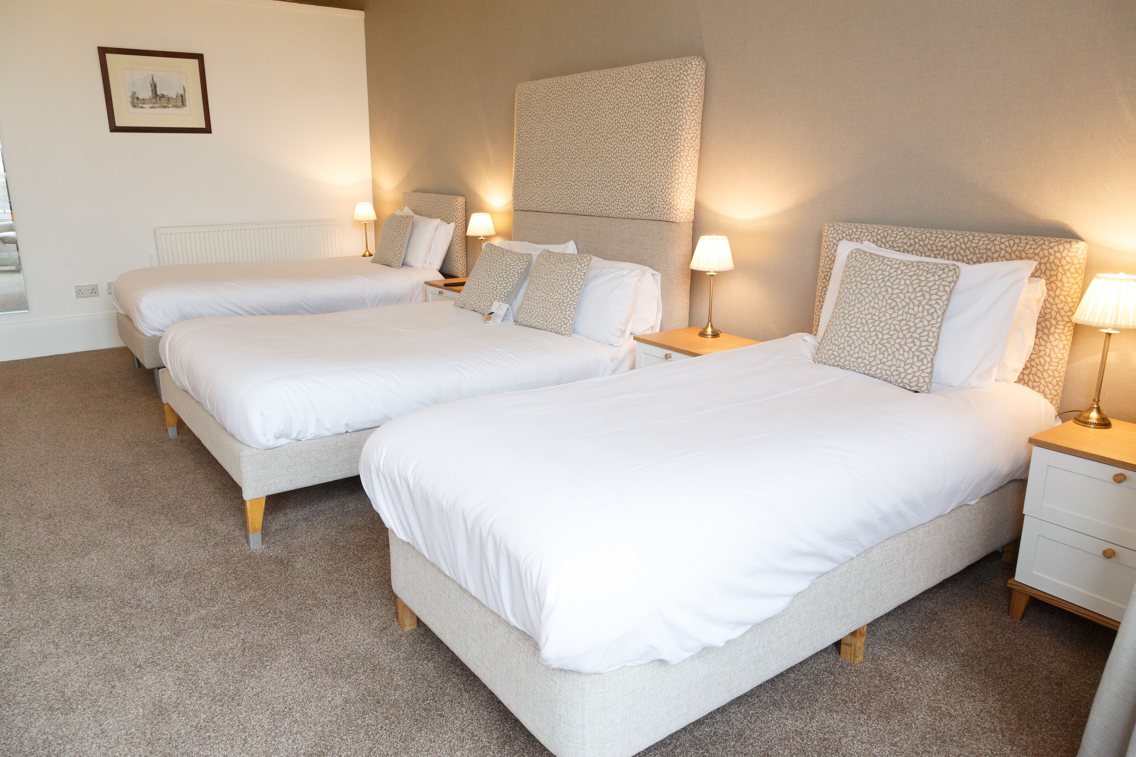 Une chambre d’hôtel avec deux lits, chacun doté d’une table de chevet et d’une lampe, d’un radiateur et d’un tableau encadré au mur.