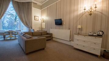 A living room with a sofa set, a TV mounted on the wall, a radiator, and a dresser with a lamp.