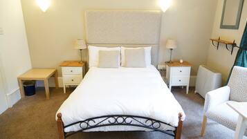 A bedroom with a bed, two bedside tables, a chair, a radiator, and wall-mounted lamps.