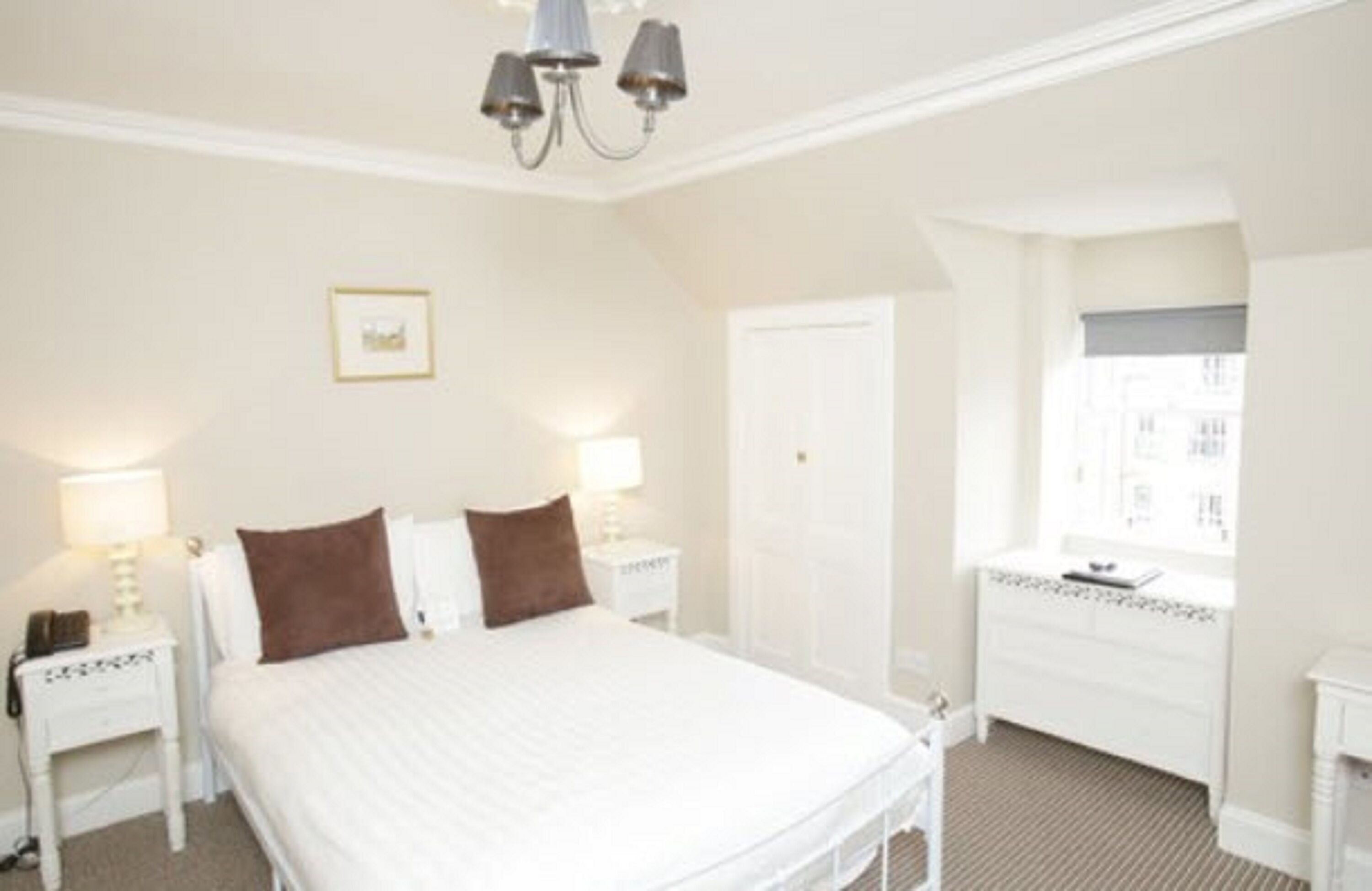 A hotel room with a bed, bedside tables, a nightstand, a dresser, and a window.