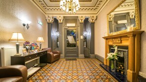 Un hall d’hôtel avec un sol à motifs, une cheminée, un miroir et un lustre.