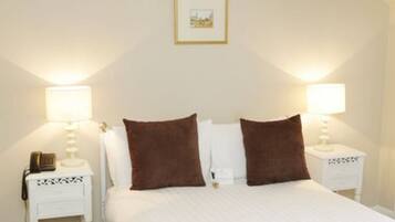 A neatly made bed with two brown pillows and white bedding, flanked by two bedside tables with lamps and a small decorative item on each.