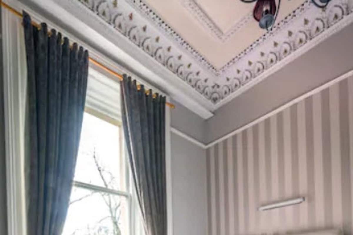 A bedroom with a large bed, striped wallpaper, and a window with curtains.