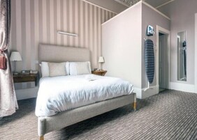 Habitación de hotel ordenada con una cama grande, una mesita de noche con lámpara, un armario y un espejo.