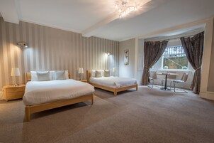 Ein Hotelzimmer mit zwei Betten, einem kleinen Tisch mit Stühlen, einem Fenster mit Vorhängen und einer Deckenleuchte.