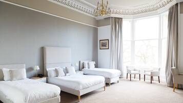 A hotel room with two beds, a chandelier, a large window with curtains, and a small table with chairs.