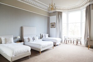 A hotel room with two beds, a chandelier, a large window with curtains, and a small table with chairs. - The Belhaven (Glasgow)