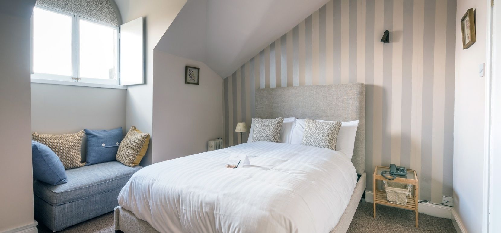 Un dormitorio con una cama grande, un sofá, una mesita de noche con lámpara y una ventana.