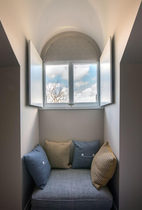 A corner room with a built-in bench, a window with a view of trees, and a textured wall design. - The Belhaven (Glasgow)