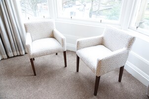 Two armchairs with a patterned fabric, positioned in front of a window with a view of a street and buildings.