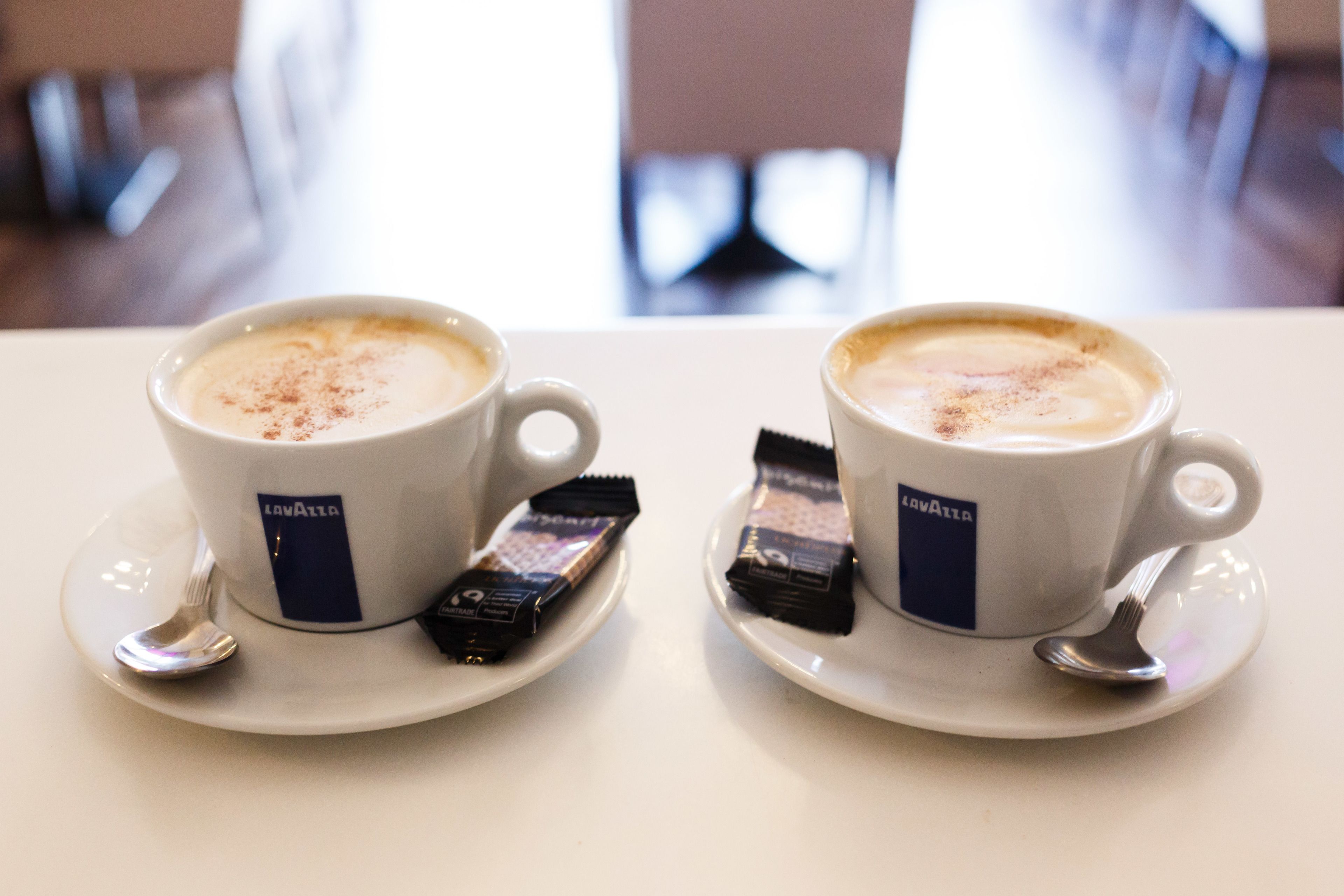Deux tasses blanches ornées d’un logo, chacune contenant une barre de chocolat et une cuillère posée sur une soucoupe.