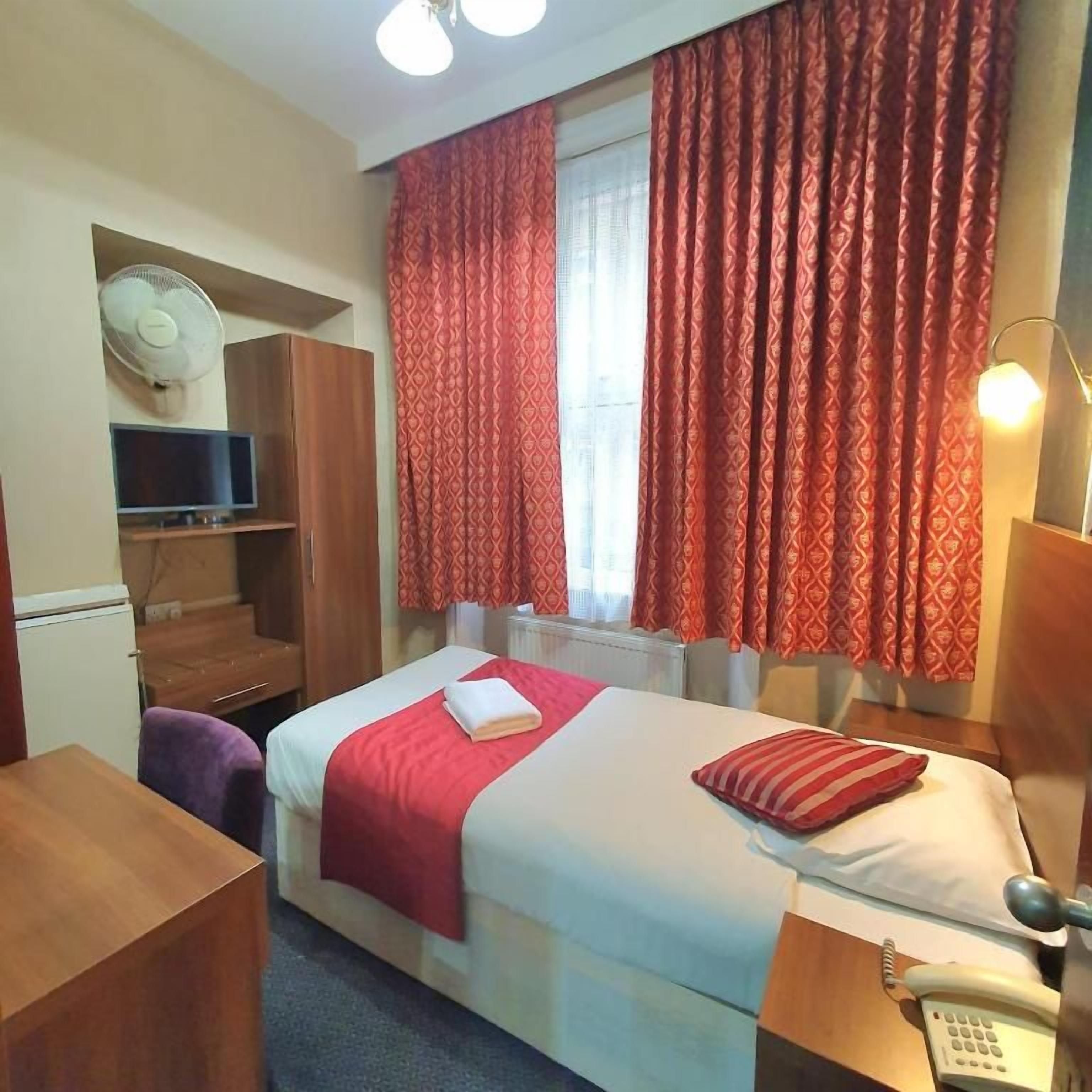 A hotel room with a bed, a desk, a chair, a TV, a phone, and a window with curtains.