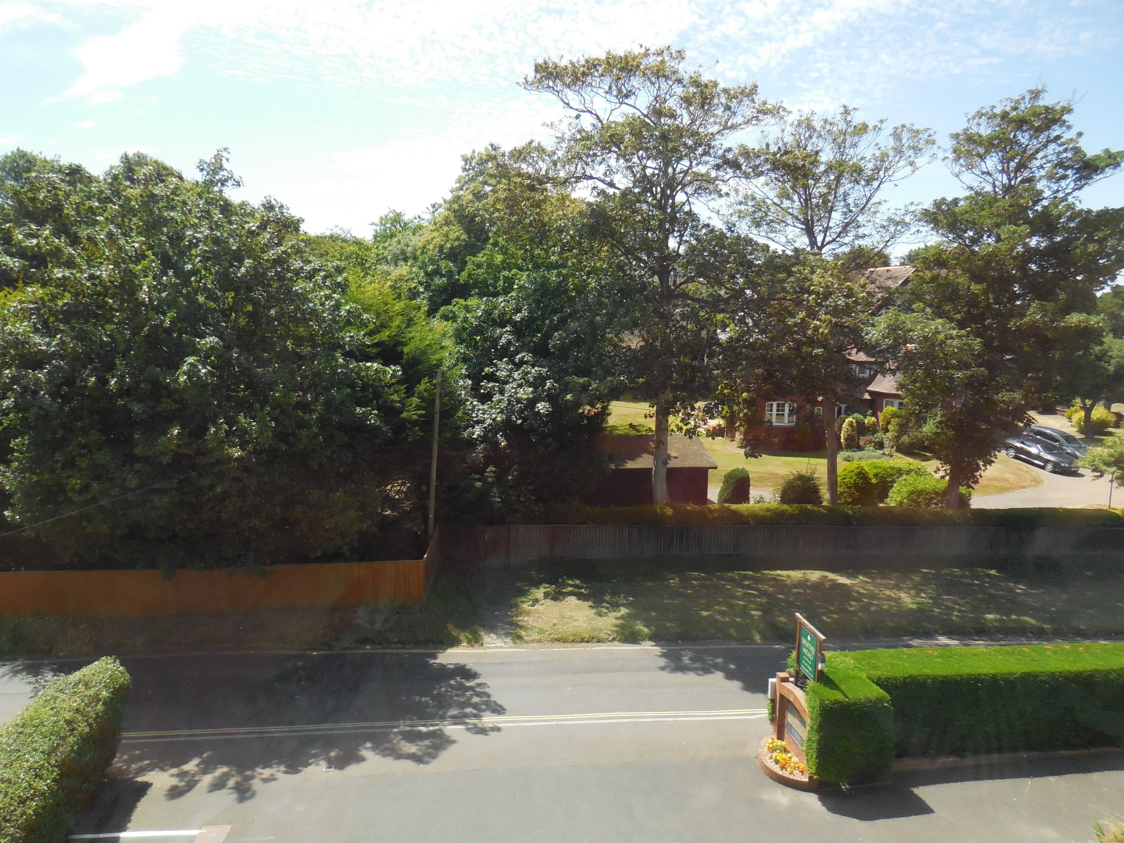 A road with a signboard, greenery, and houses in the background.