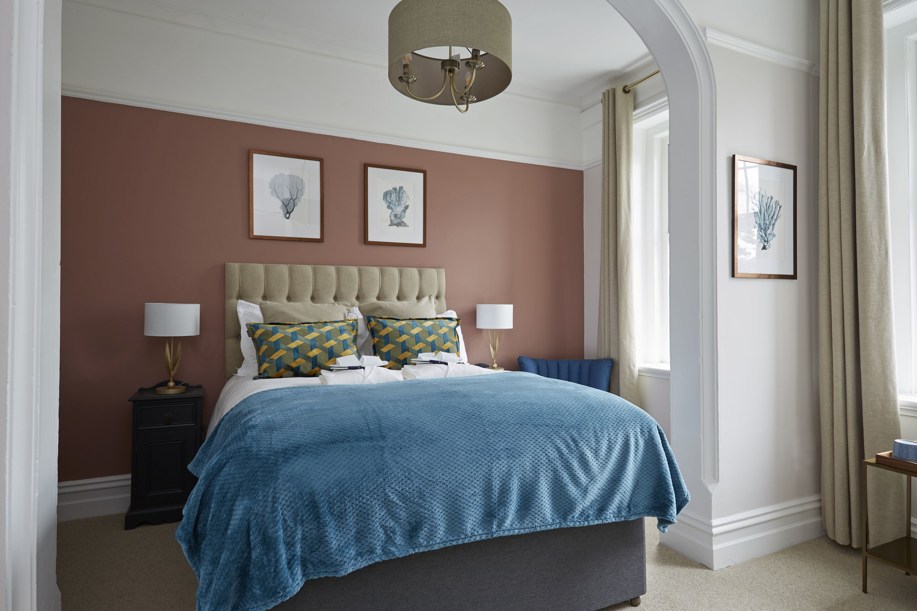 Une chambre à coucher avec un grand lit, deux tables de chevet, un lustre et des œuvres d’art encadrées accrochées aux murs.