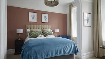 Une chambre à coucher avec un grand lit, deux tables de chevet, un lustre et des œuvres d’art encadrées accrochées aux murs.