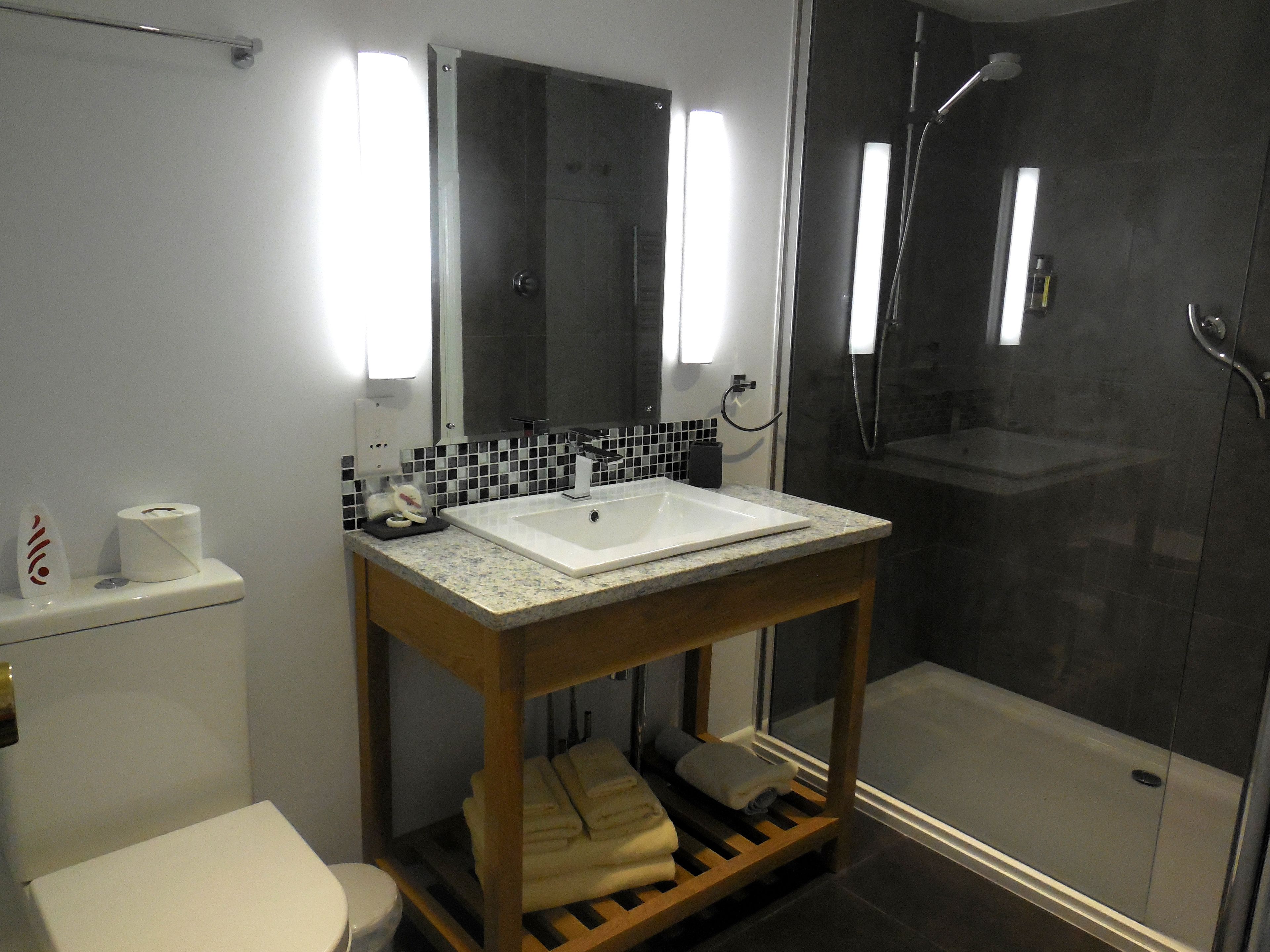 A bathroom with a white sink, black and white tiled backsplash, a mirror, a toilet, and a shower area.