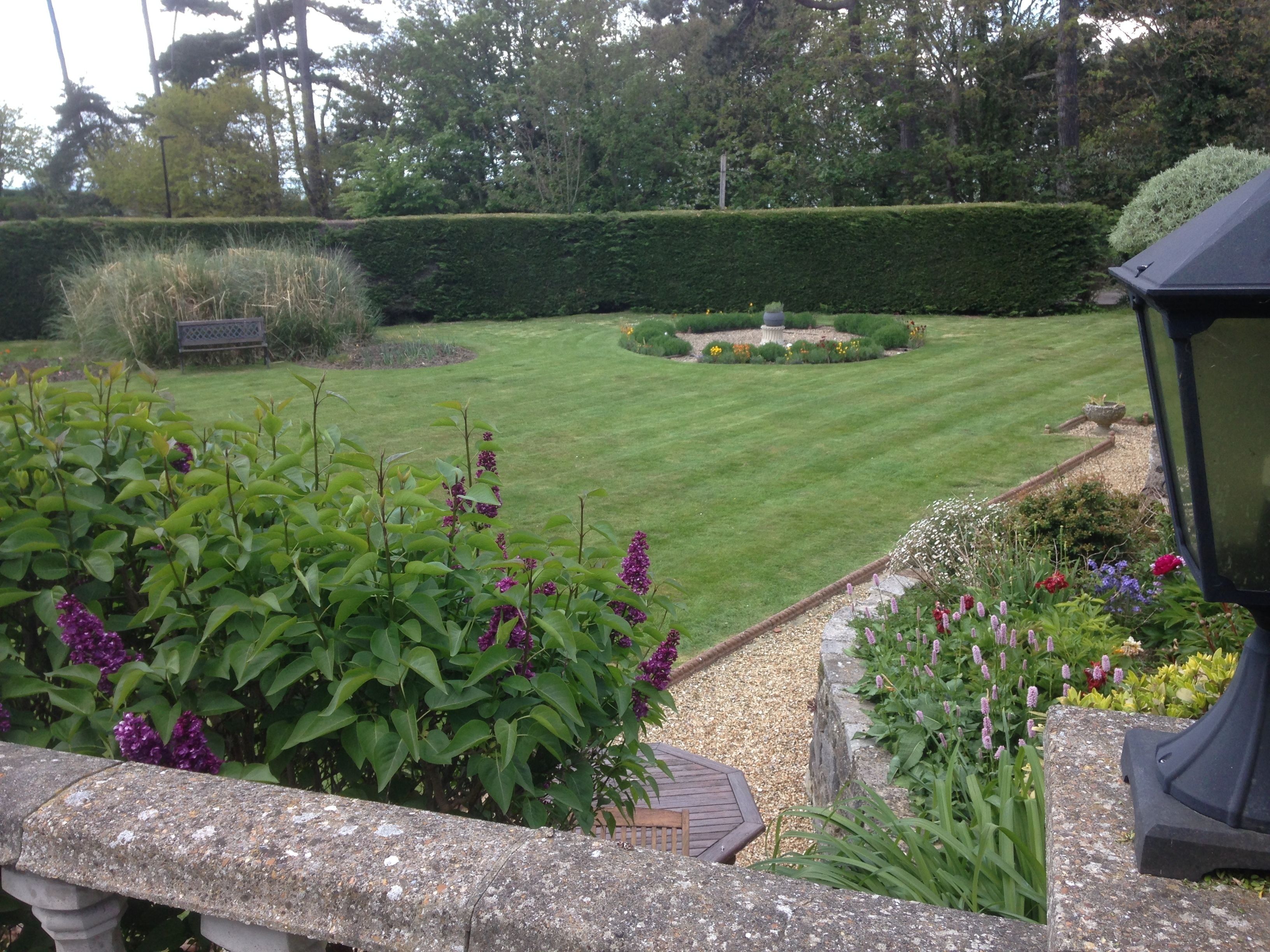 A well-maintained garden with a lawn, a stone bench, and a variety of flowering plants.