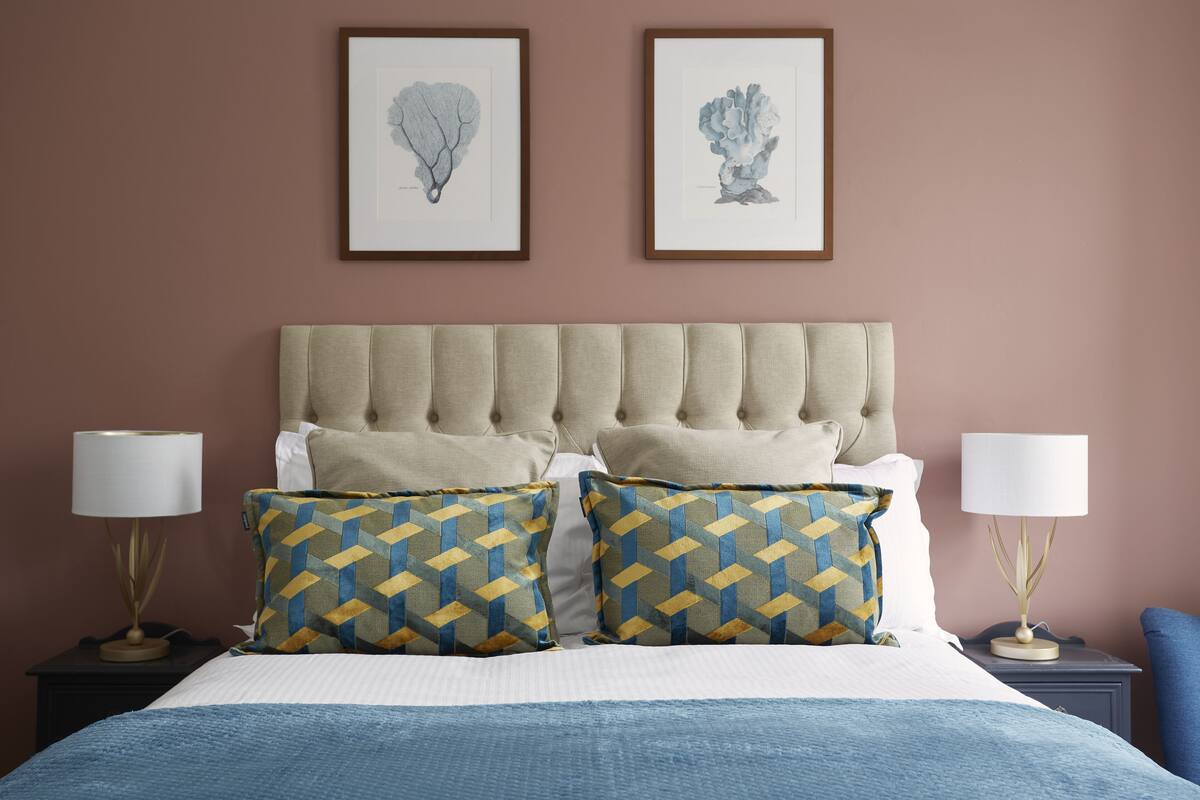 Quarto com cabeceira estofada, duas mesas de cabeceira com luminárias, cama com almofadas estampadas e duas obras de arte emolduradas na parede.