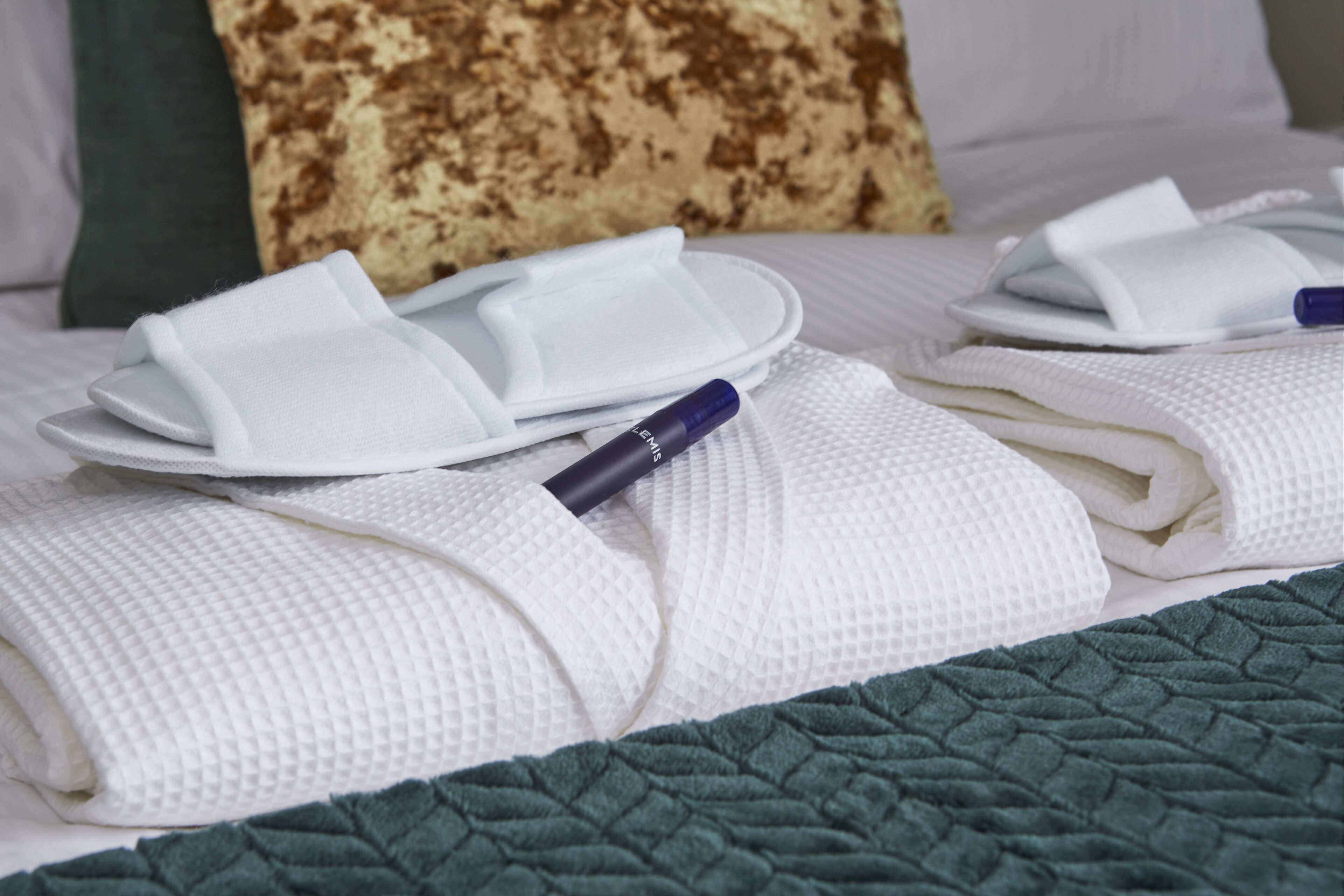 A neatly made bed with white towels, a green blanket, and a blue pen on the bed.
