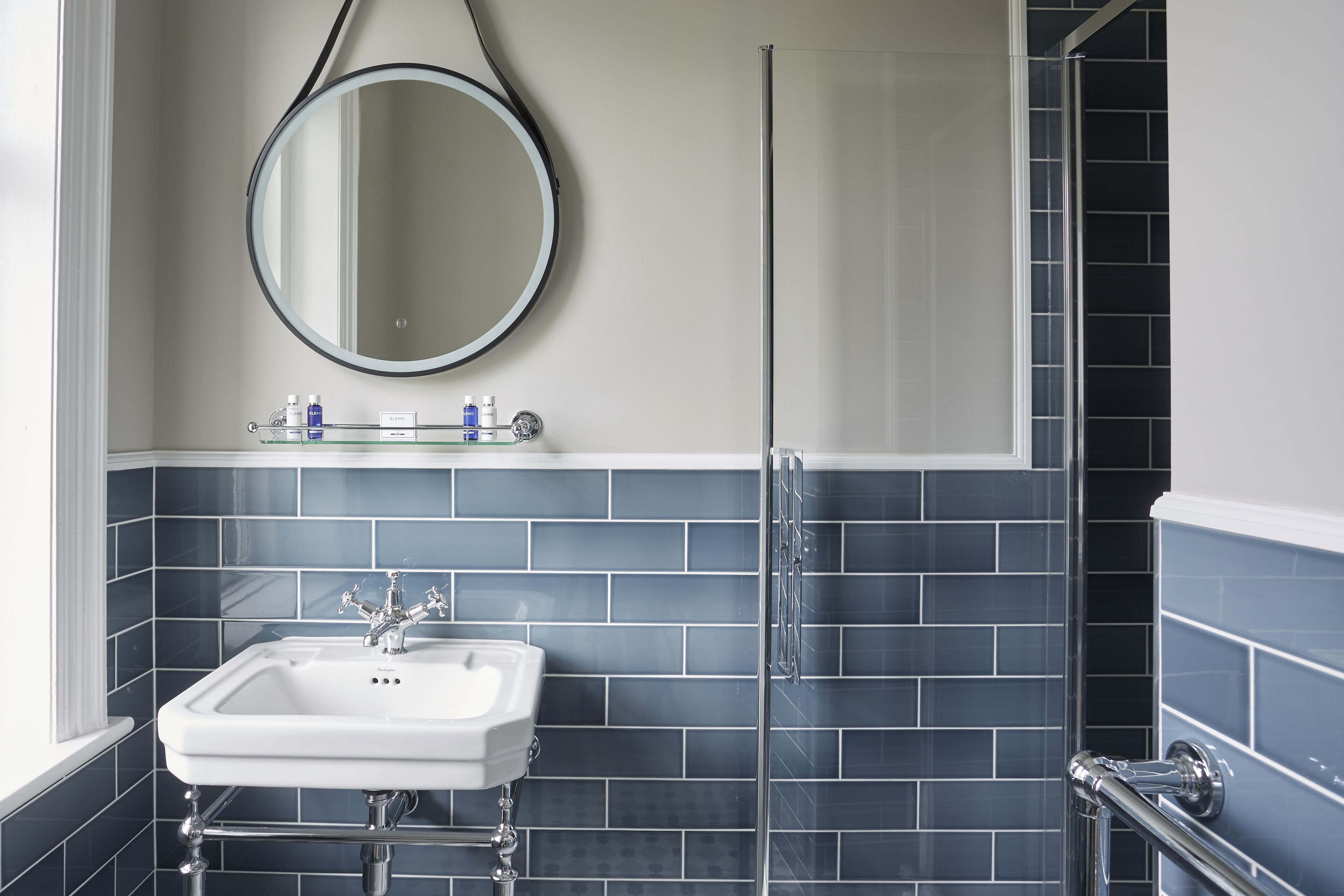 Une salle de bain avec un lavabo blanc, un miroir rond et une cabine de douche en verre.