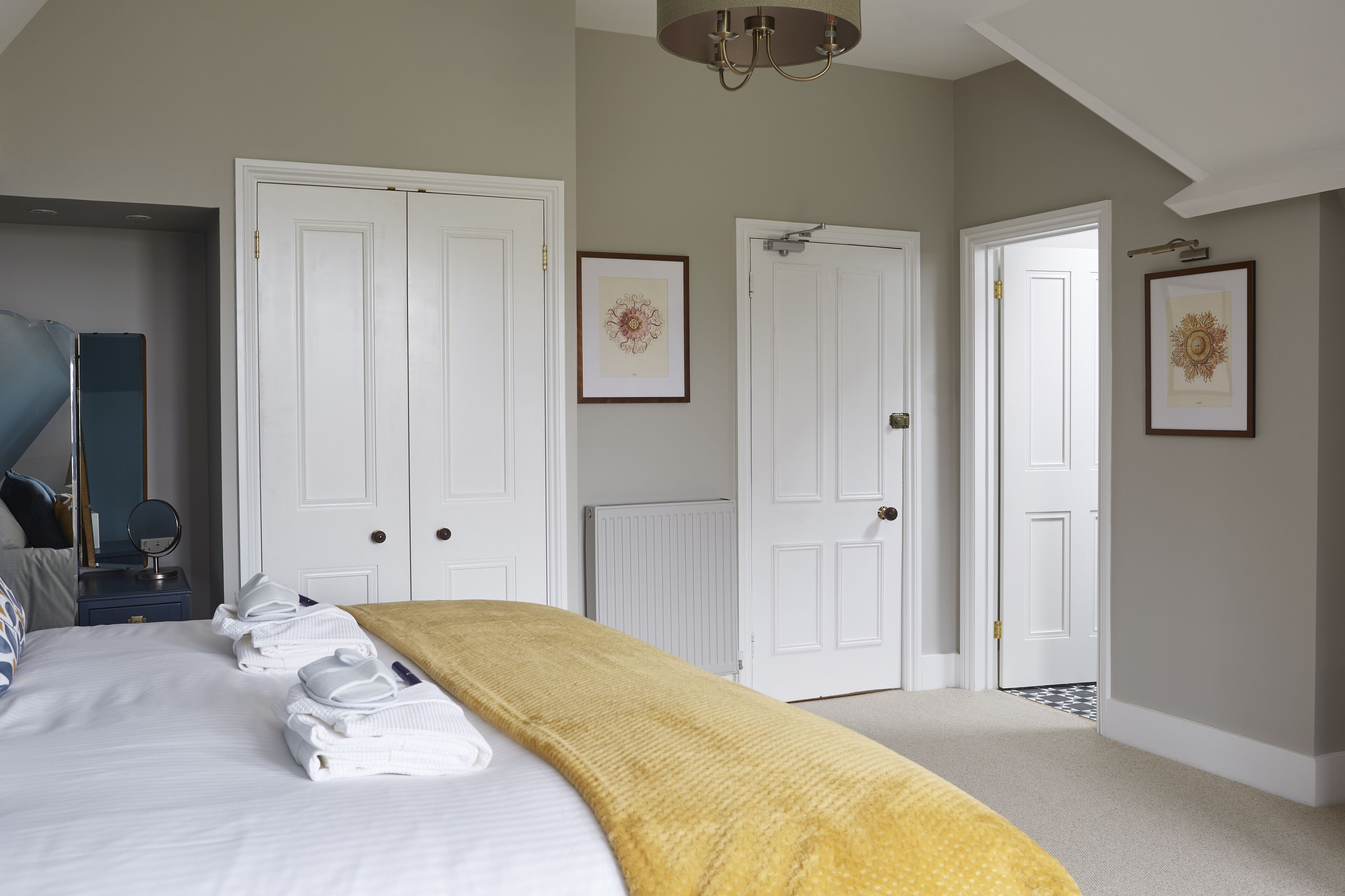 A neatly made bed with towels, white doors, and framed artwork on the walls.