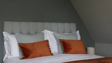 A neatly made bed with a grey upholstered headboard, white and orange pillows, and a brown throw blanket.
