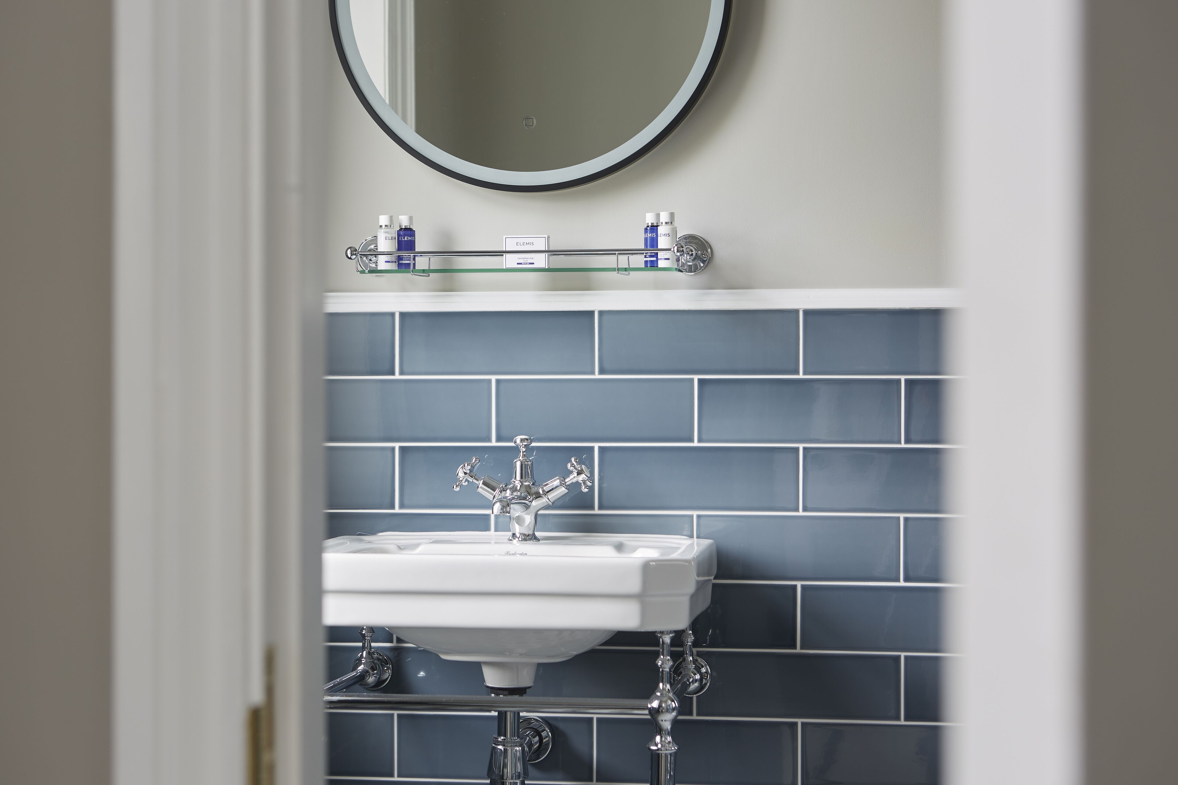 A bathroom with a white sink, blue tiles, and a mirror above it.