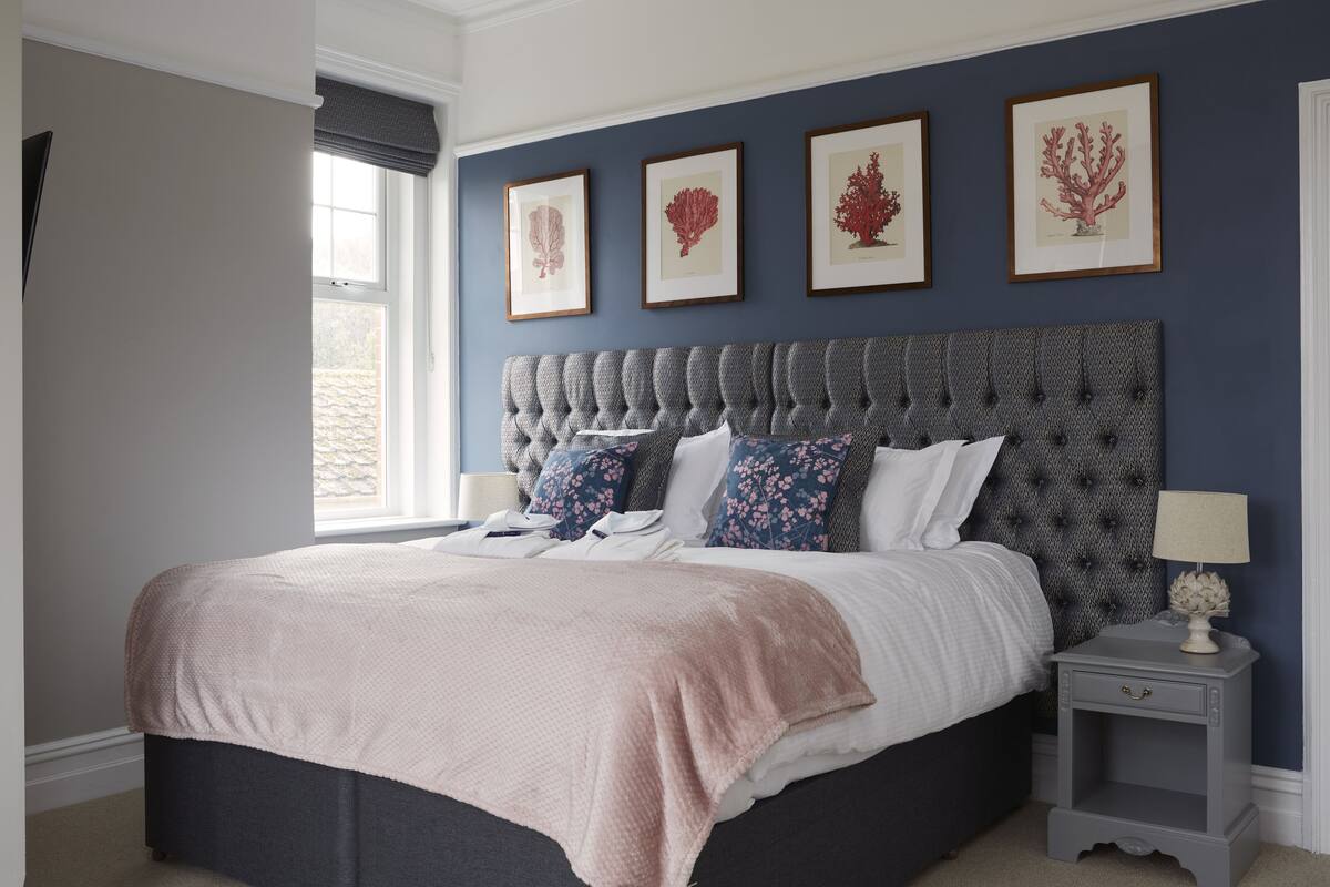 Quarto com uma cama grande, uma mesa de cabeceira e impressões botânicas emolduradas na parede.