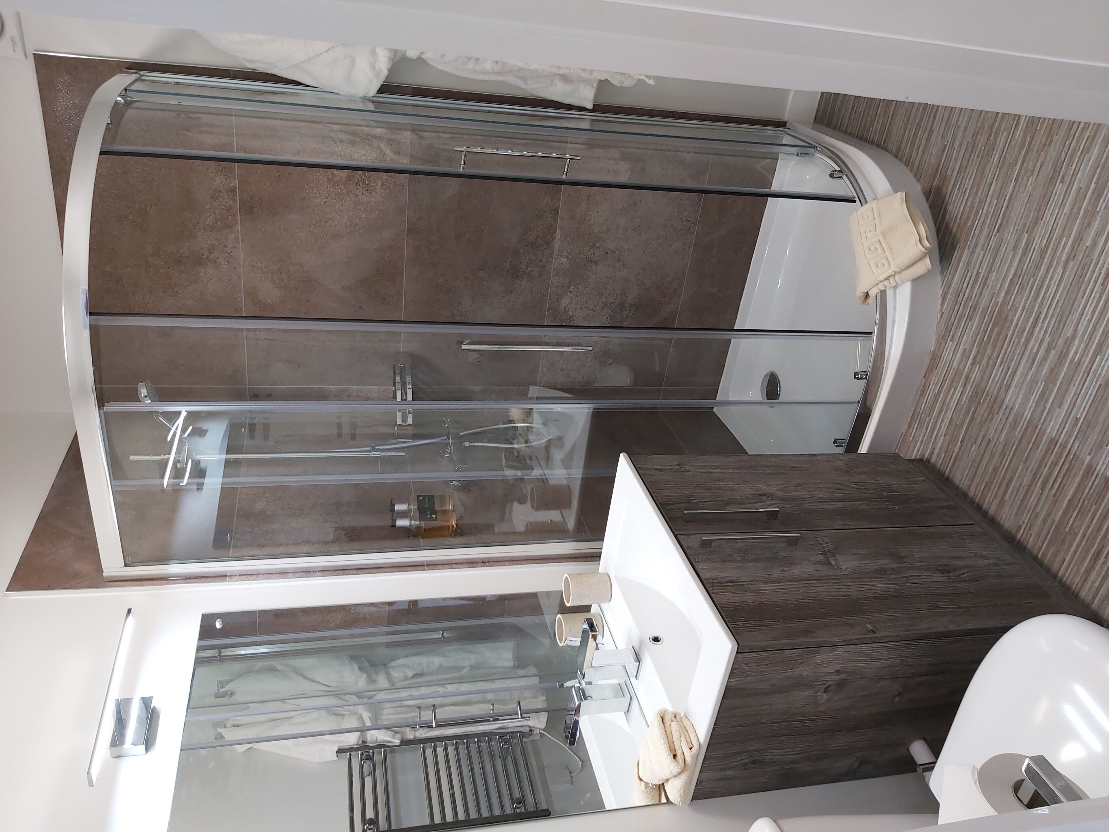 A modern bathroom with a glass-enclosed shower, a wooden vanity, and a white sink.