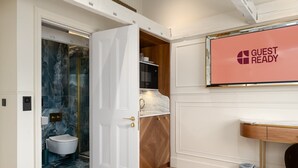 A hotel bathroom with a marble wall, a white toilet, a shower, and a sink with a towel rack. - Fitzroy (London)