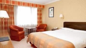 Una habitación de hotel con una cama, dos sillas, una mesita y un escritorio.