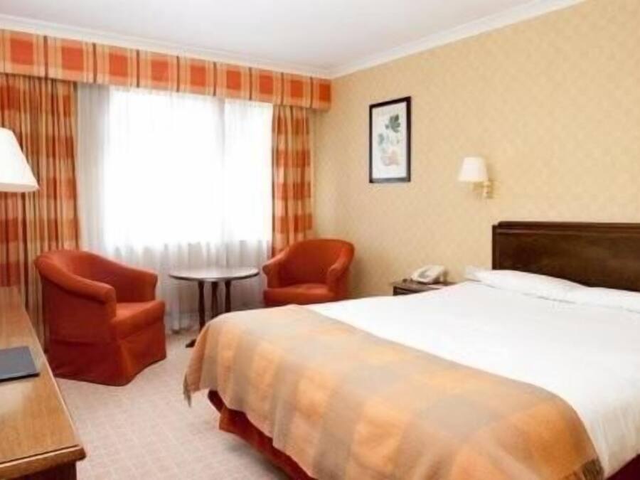 Una habitación de hotel con una cama, dos sillas, una mesita y un escritorio.