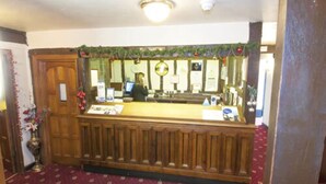 A reception area with a wooden counter, a clock, and a person behind it. - The Roebuck Inn (Stevenage)